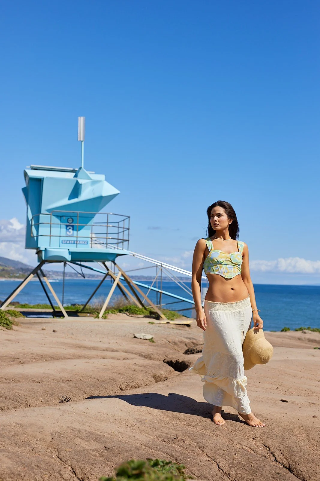 Model posing on a beach front near a blue lifeguard booth