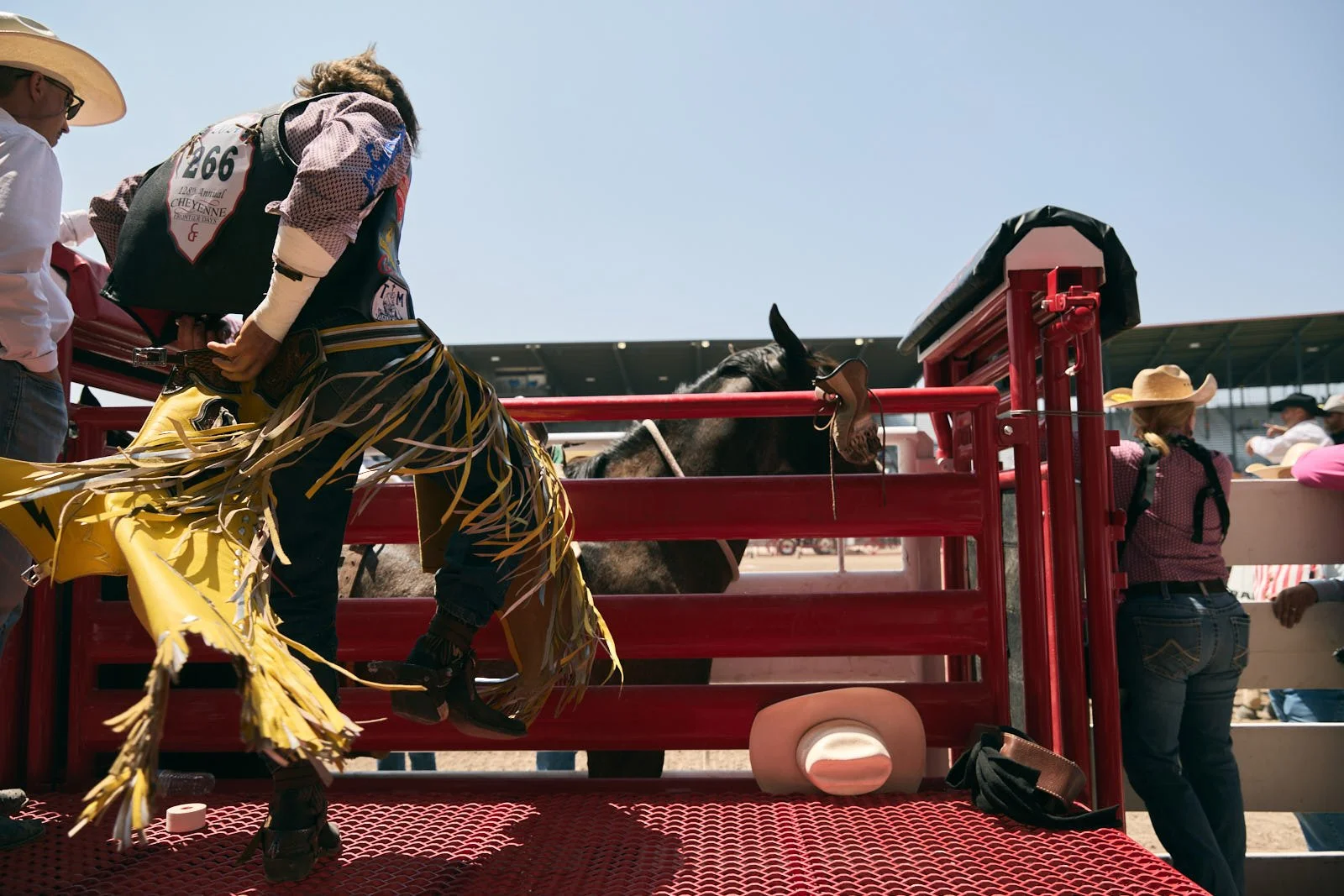 Cowboy adjusting his yellow chaps on a red cattle chute platform at a rodeo