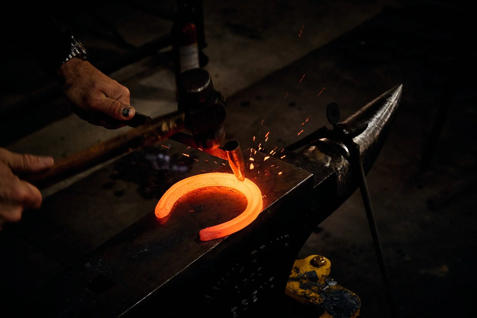 Farrier forging a horseshoe on an anvil, with sparks flying as the red-hot horseshoe is shaped.