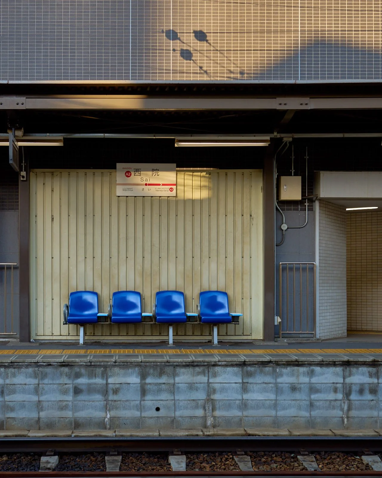 Empty blue seats at a train station platform with a sign and parking area behind.