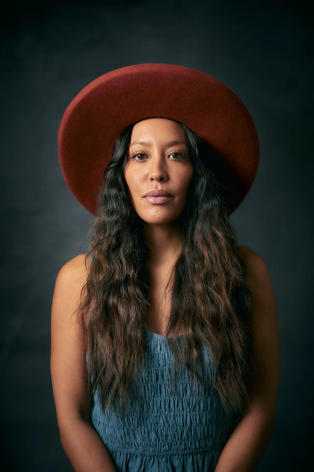 Model wearing a large brim red hat in front of a dark background