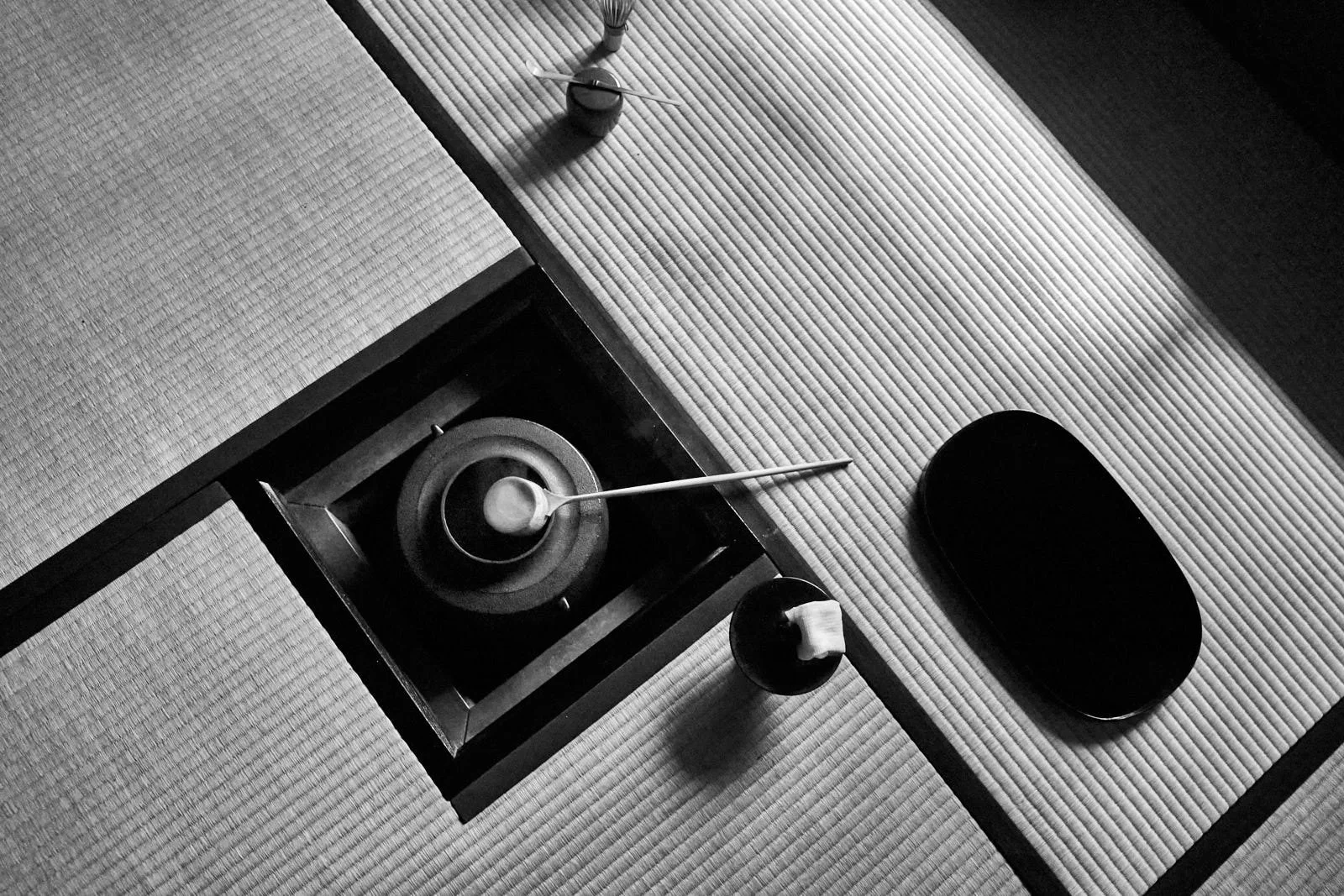 A traditional Japanese tea setting with a tea kettle, bowls and utensils on tatami mats.
