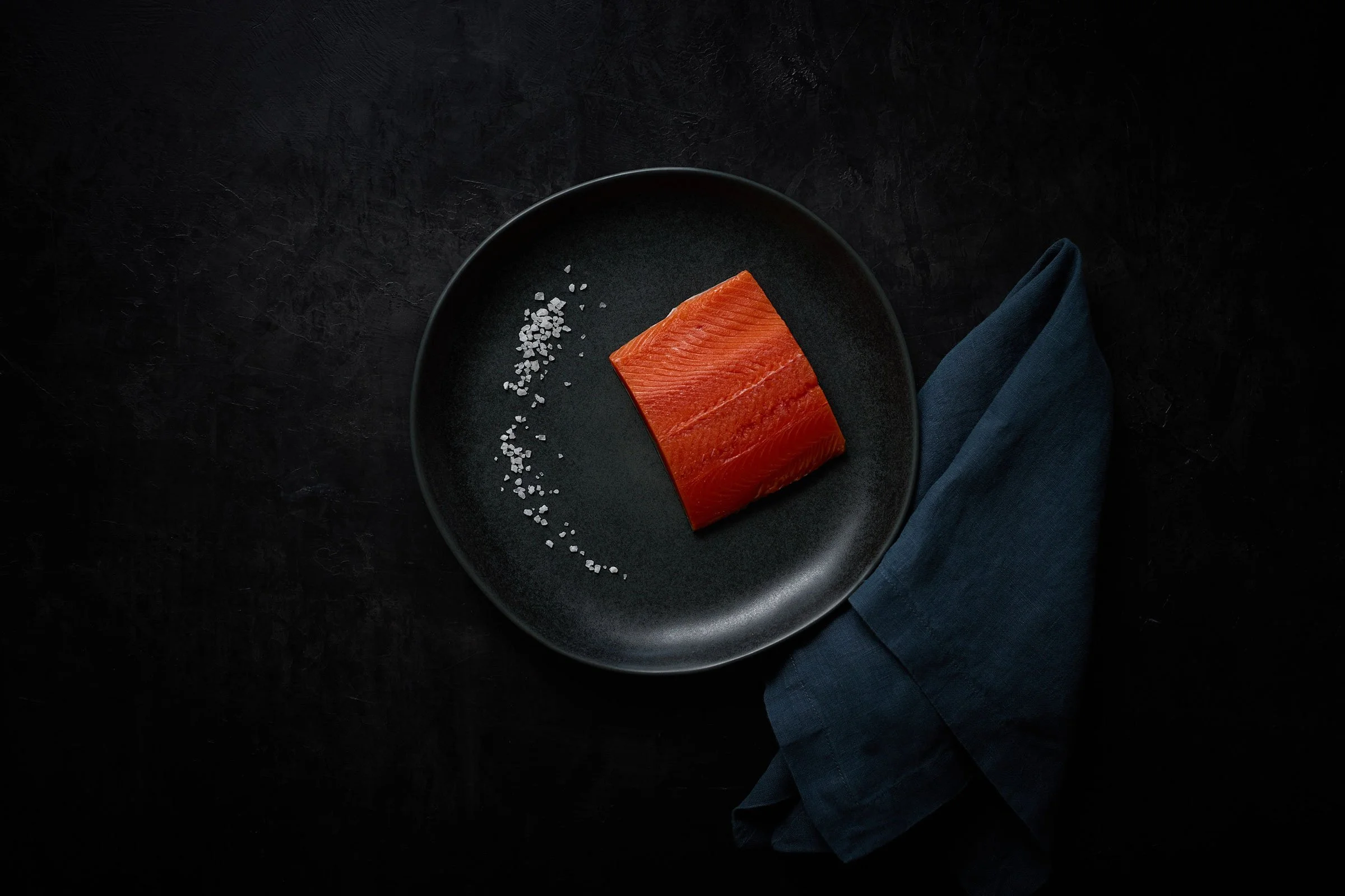 Top down view of a raw salmon filet on the dark plate and dark background