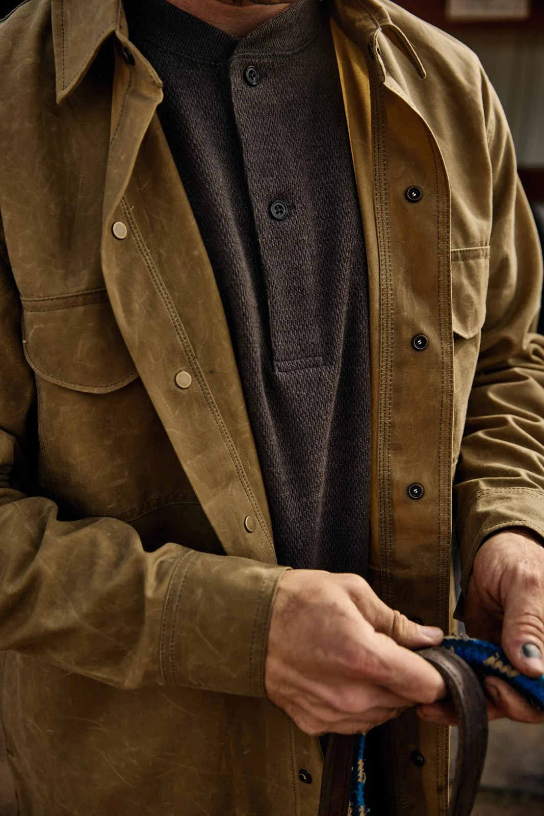 A person wearing a brown jacket over a dark gray or black button-up shirt, holding a horse lead.