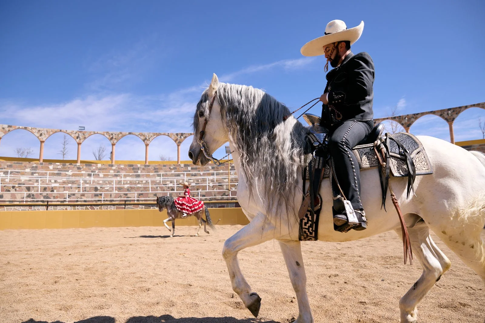 A man dressed in traditional Mexican attire riding a white horse in an arena.