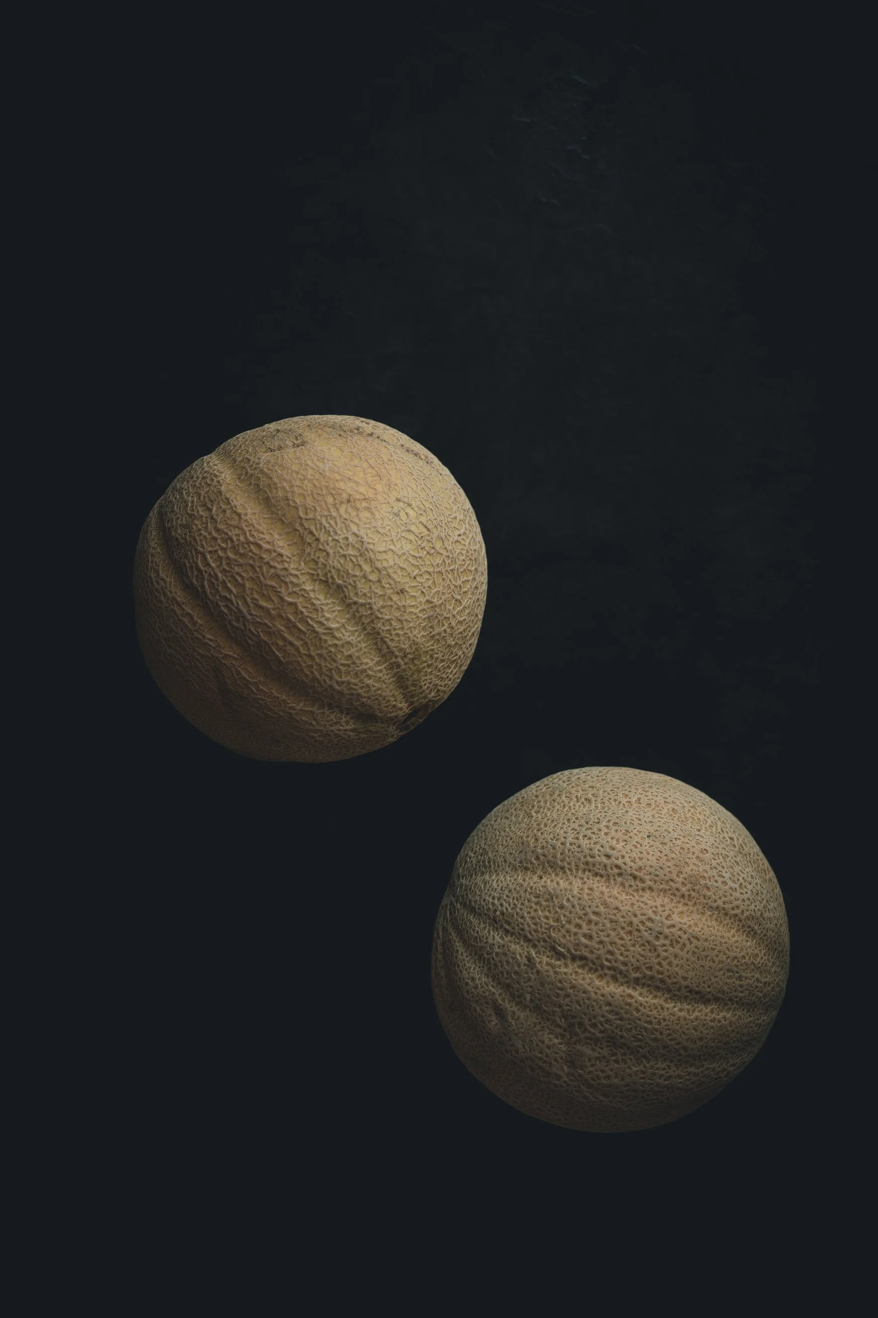 Two cantaloupe melons on a dark surface.