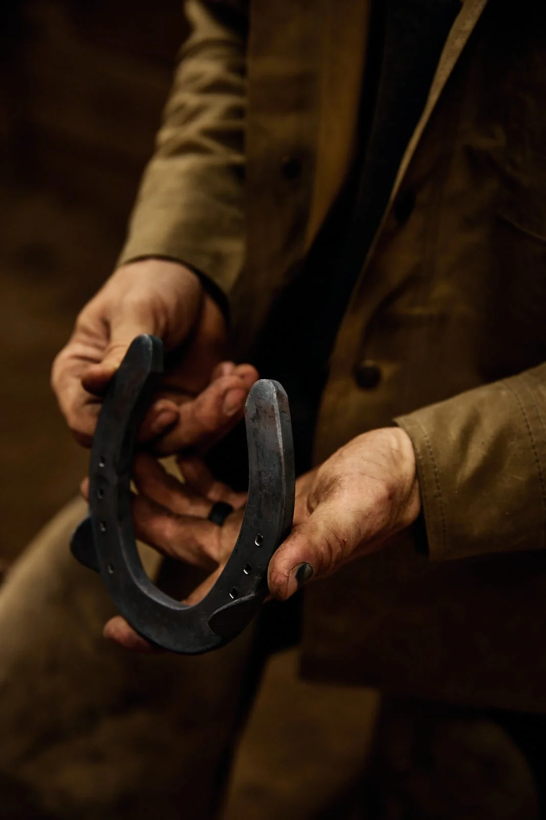 Person holding a horseshoe with dirty hands, wearing a brown jacket.