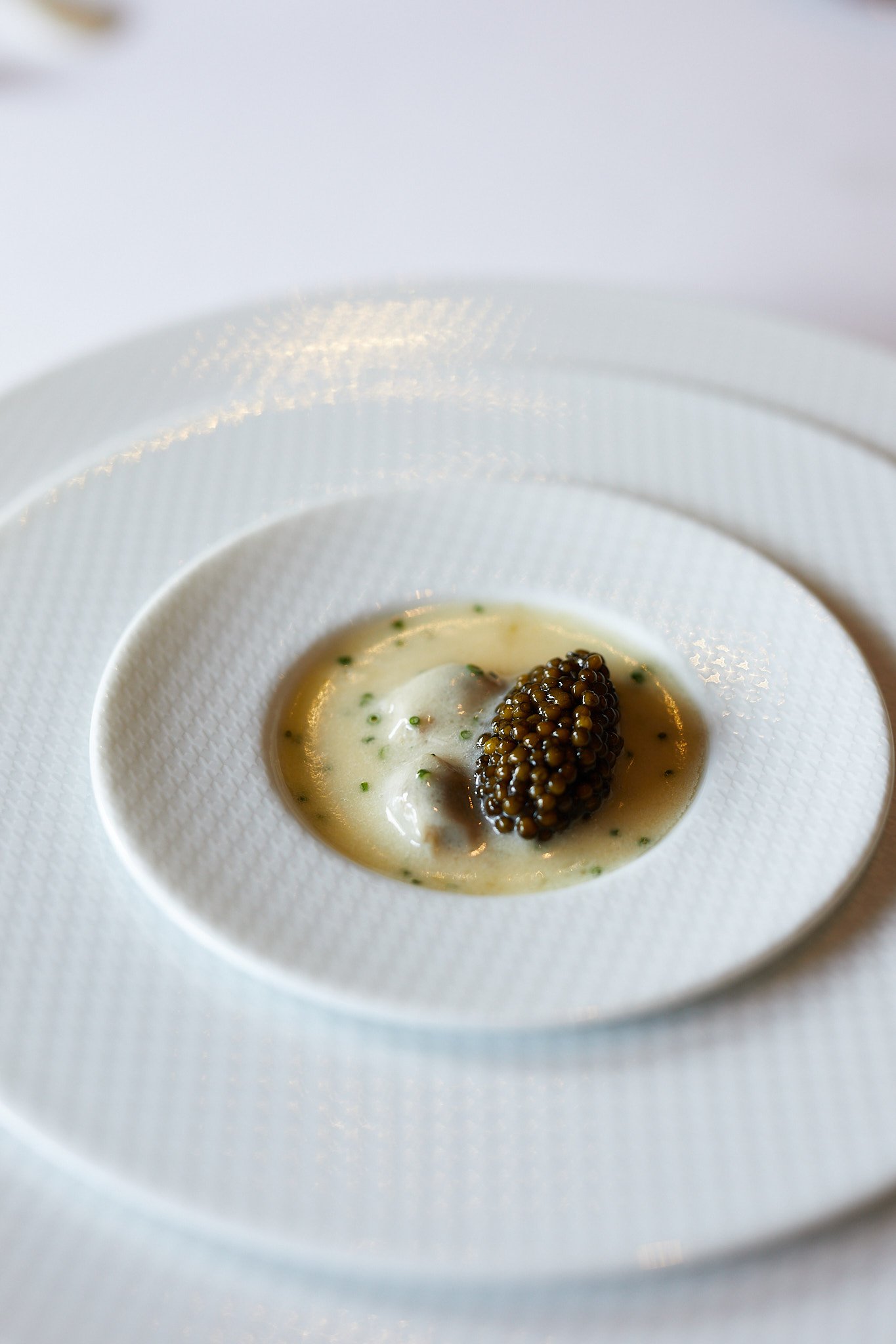 Close-up of a gourmet dish with a white creamy sauce, topped with a cluster of black caviar, presented on a textured white plate.