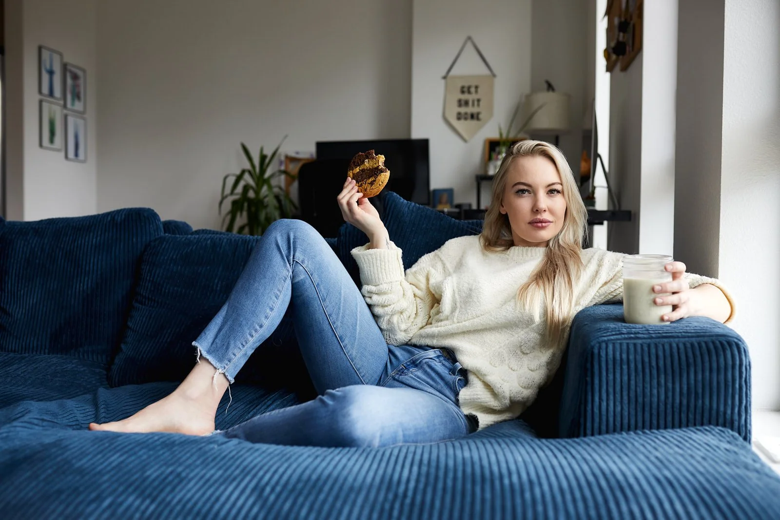 Model lounging on a blue couch with milk and a large cookie in a Denver, CO apartment