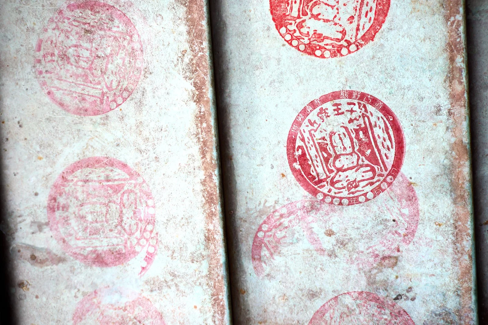 Close-up of old, weathered paper with red Japanese stamps featuring traditional Japanese characters and imagery.