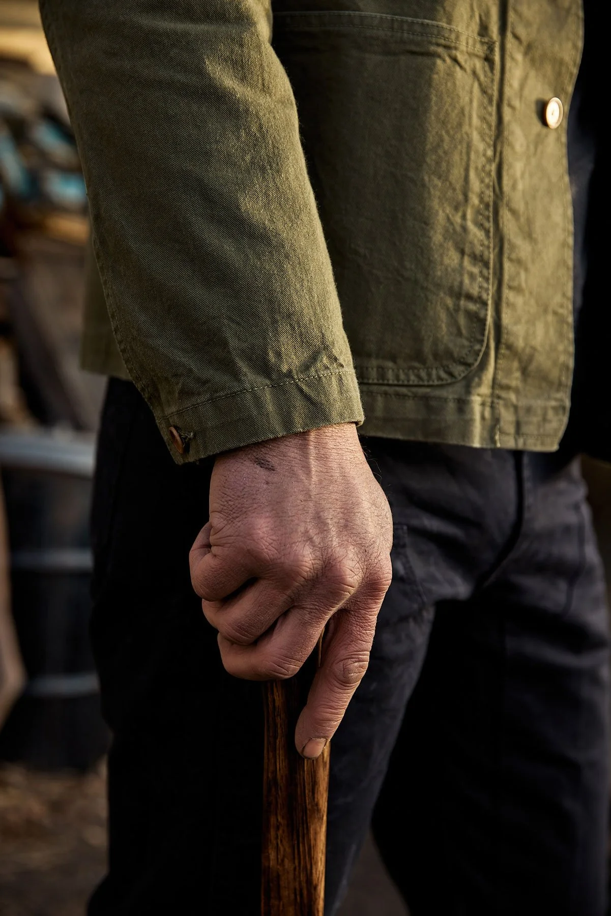 Close-up of a man hand gripping a wooden axe handle, wearing a green jacket and black pants.