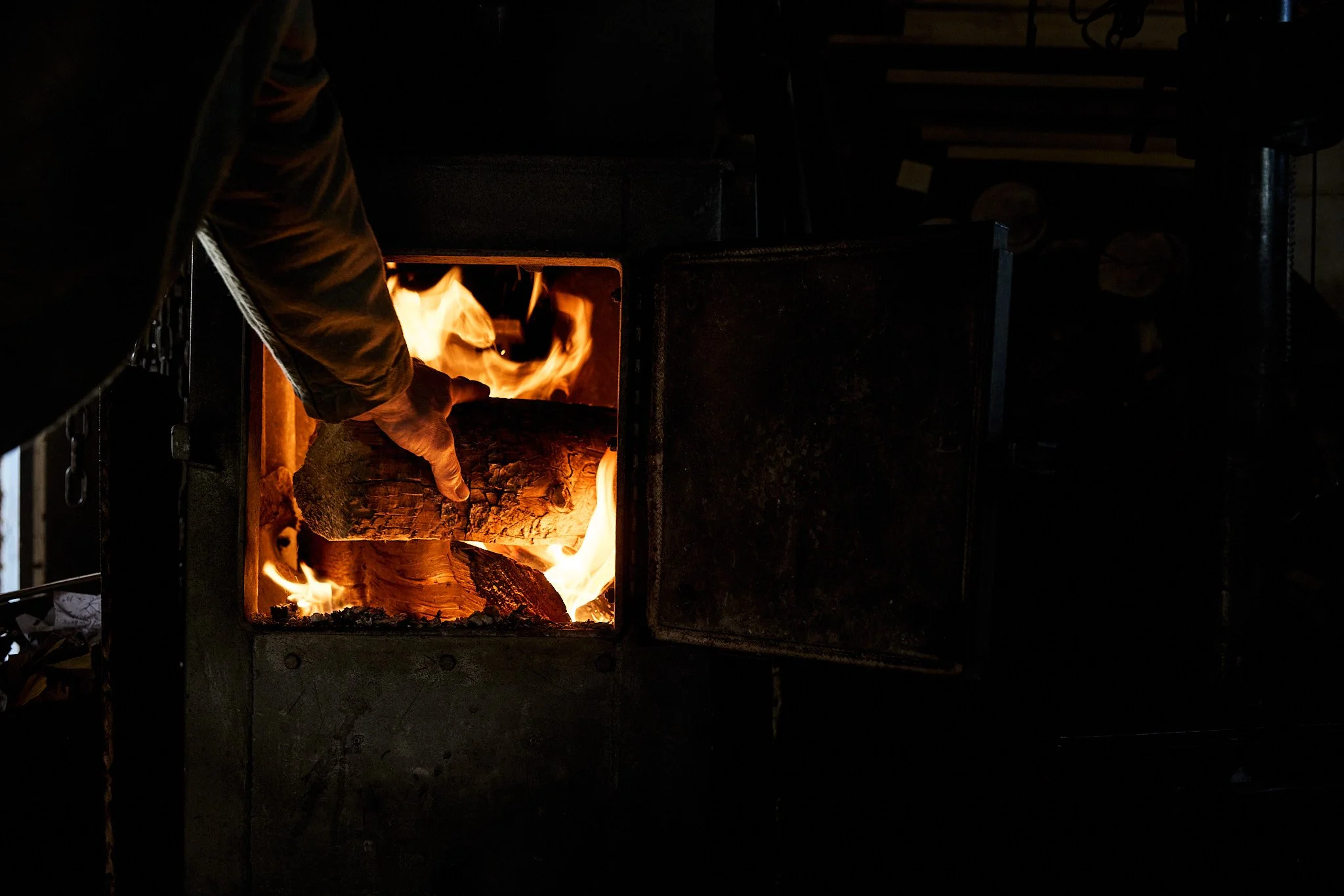 Person tending to a wood-burning stove with flames and logs inside.