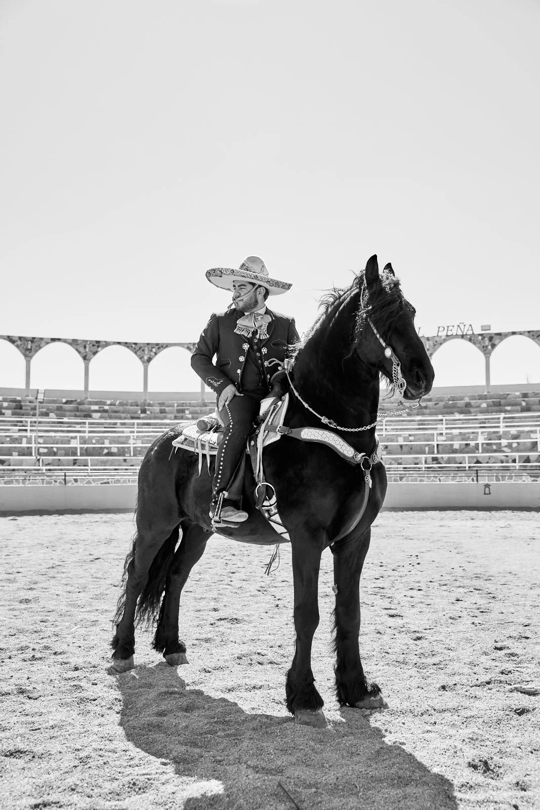 A man dressed in traditional Mexican charro attire riding a horse in an arena, with the word 'PEÑA' visible in the background.