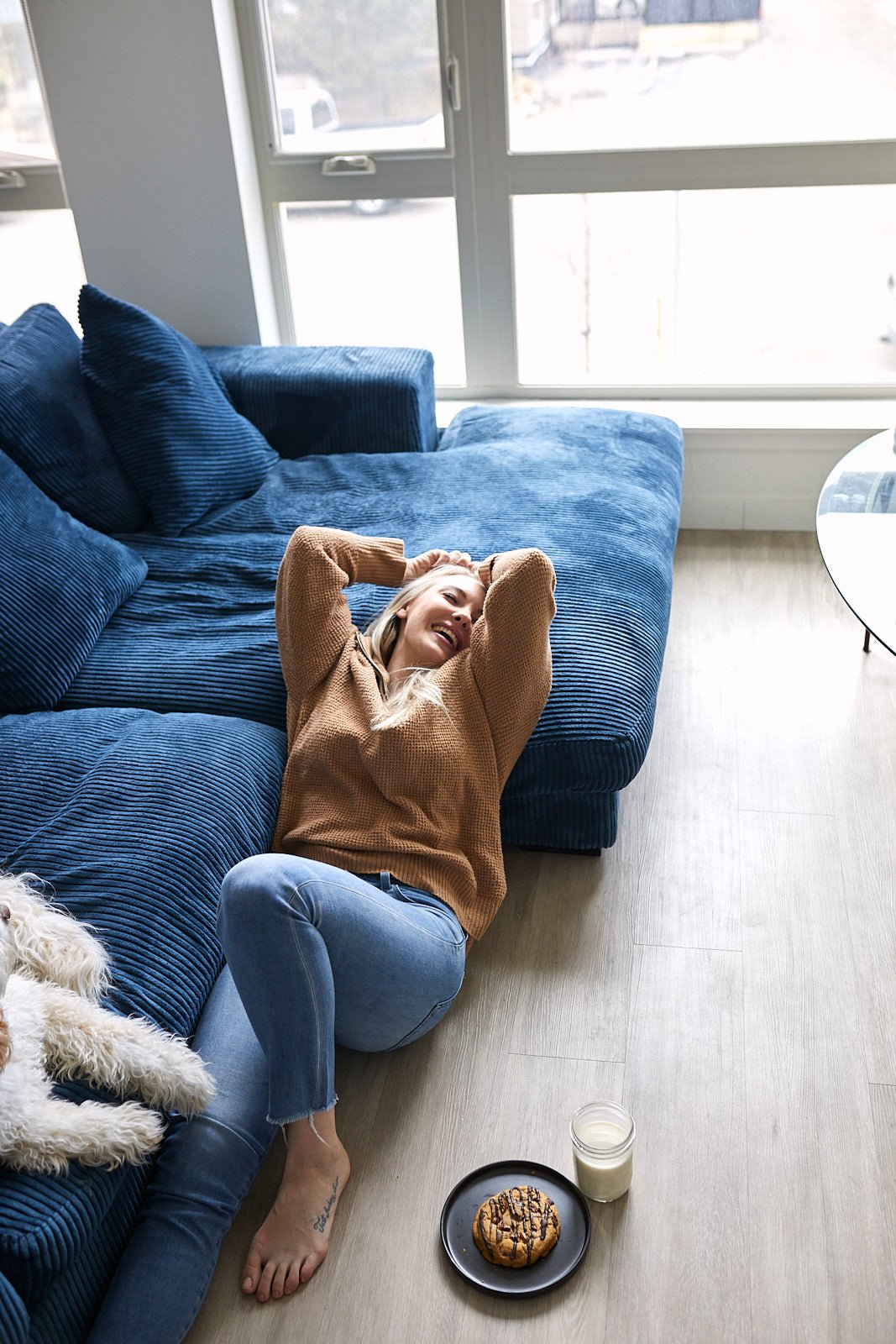 Model lounging against blue couch with her dog and a Marys Mountain cookie