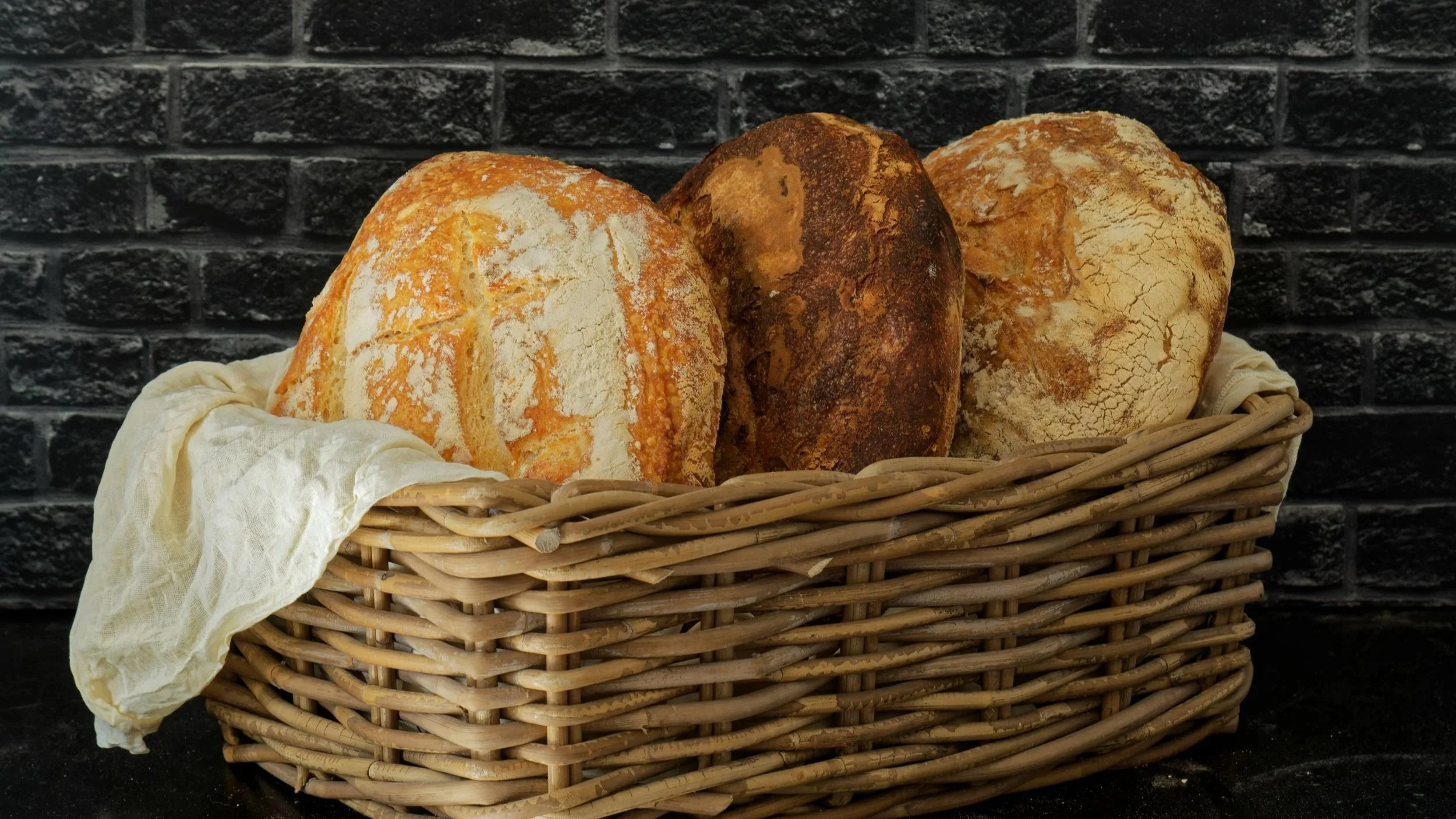 Assorted artisan bread loaves displayed in a wicker basket.