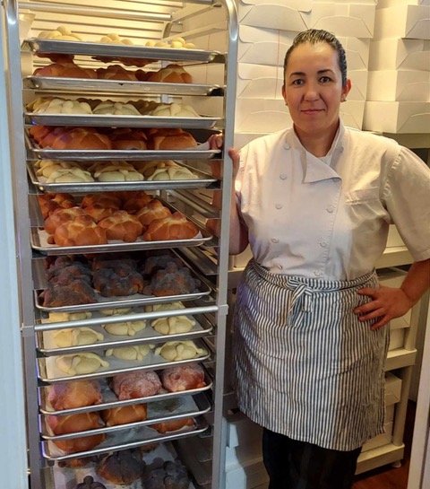 Baker Maria Duron standing beside a rack filled with freshly baked pastries.