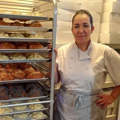 Baker Maria Duron standing beside a rack filled with freshly baked pastries.