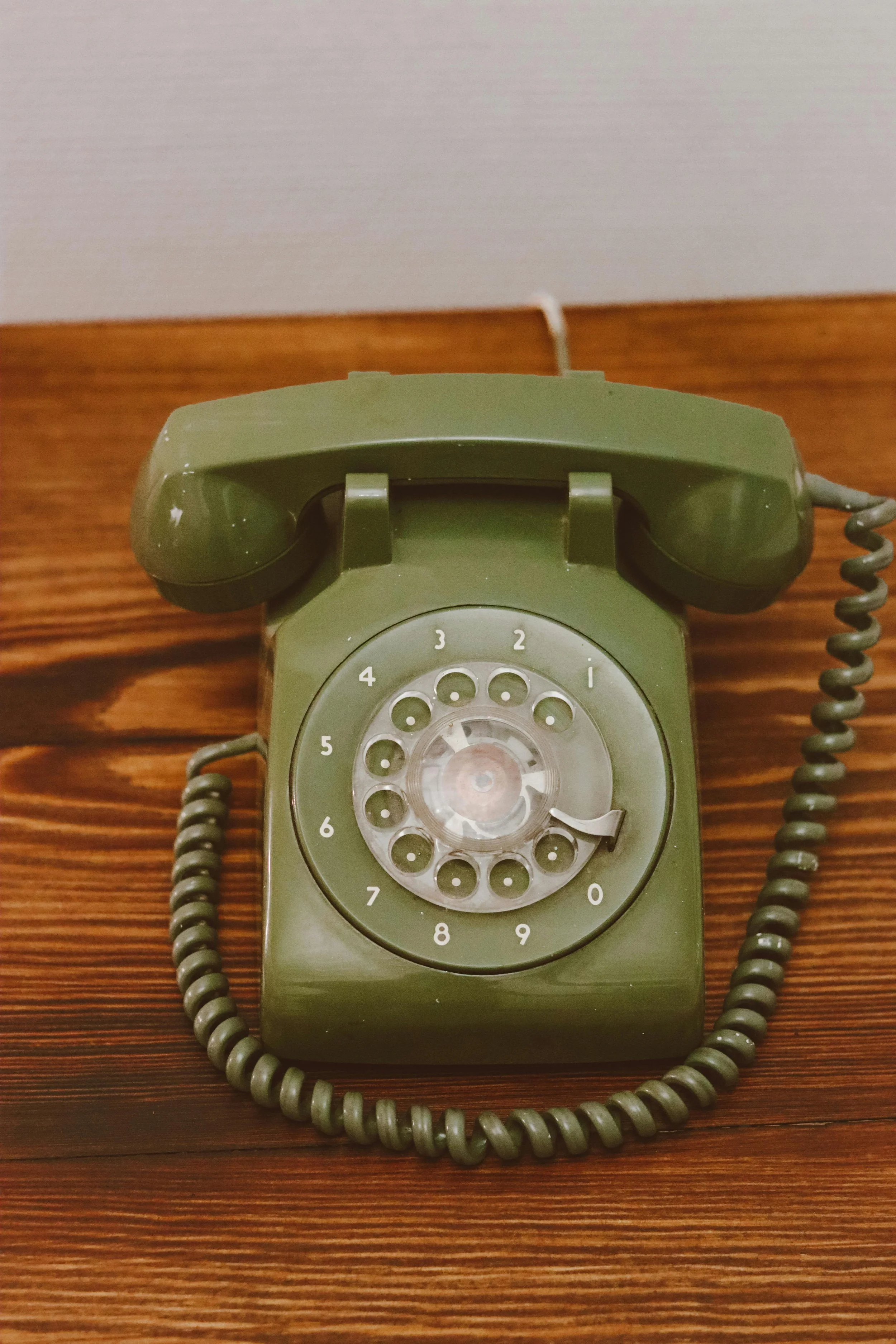 A vintage rotary telephone in olive green color placed on a wooden surface.