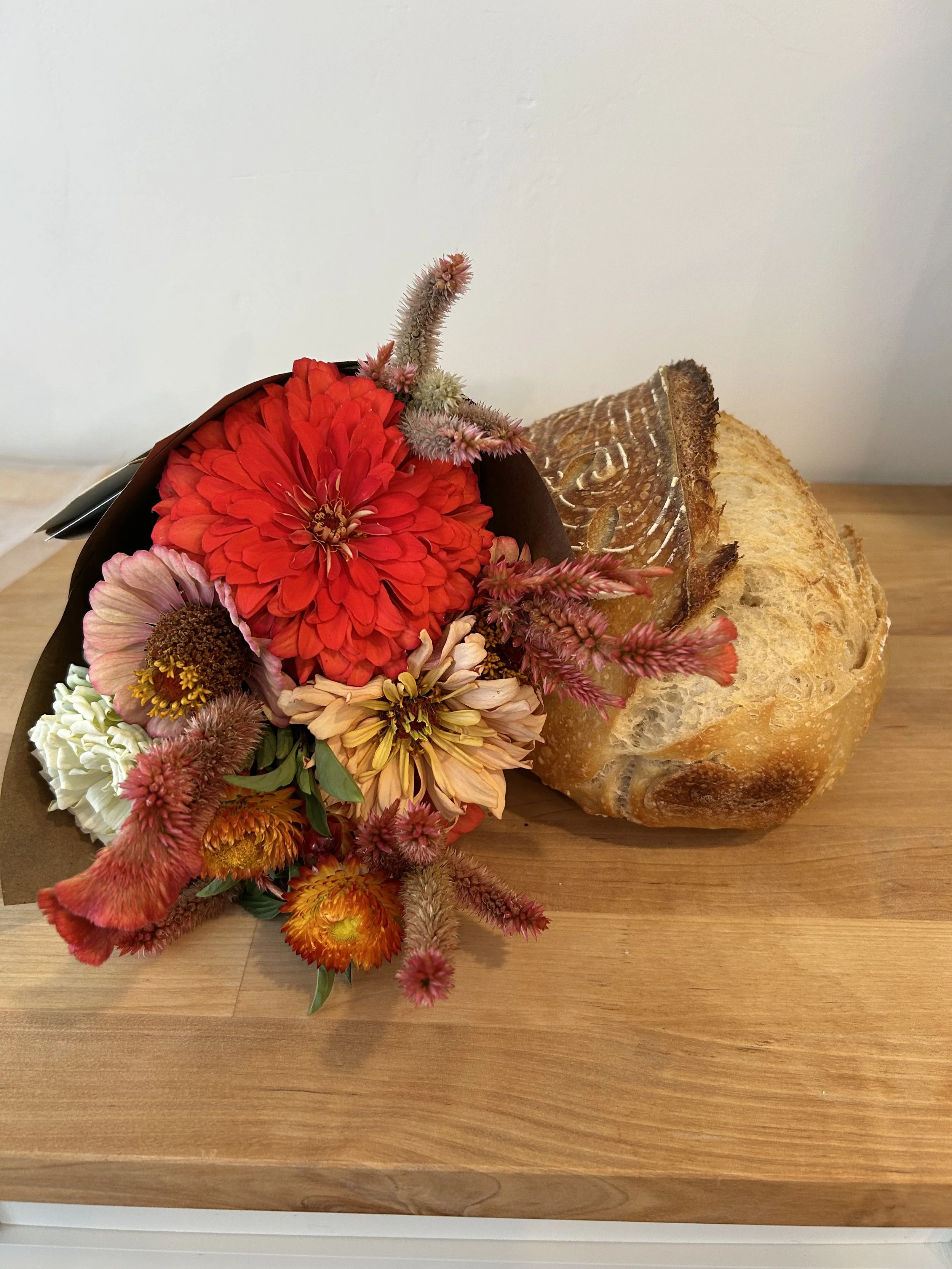 A bouquet of assorted colorful flowers and a loaf of bread on a wooden surface.