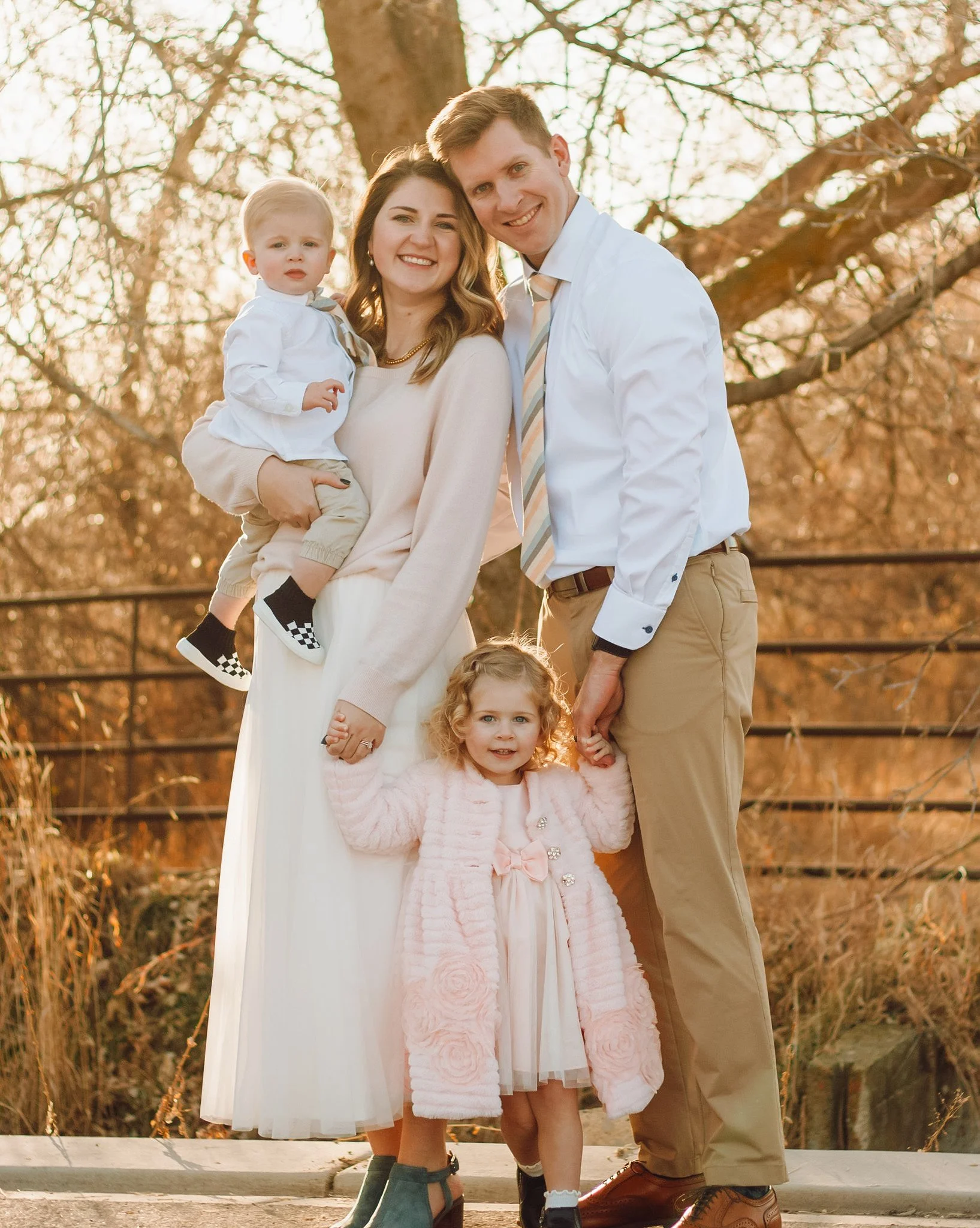 Family photo outdoors in autumn, with two parents, and two young children, all smiling.
