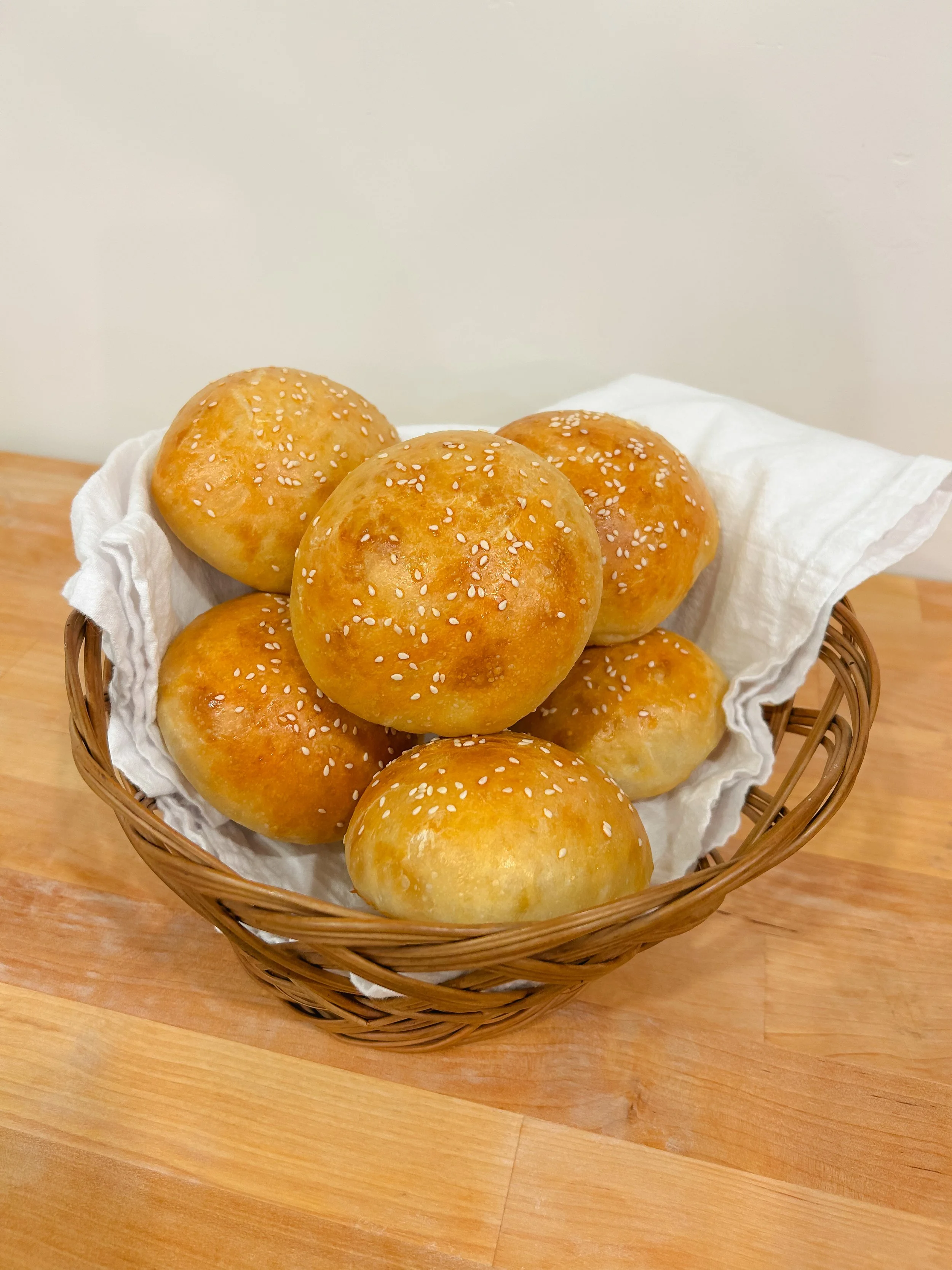 Basket of sesame seed hamburger buns on a wooden surface