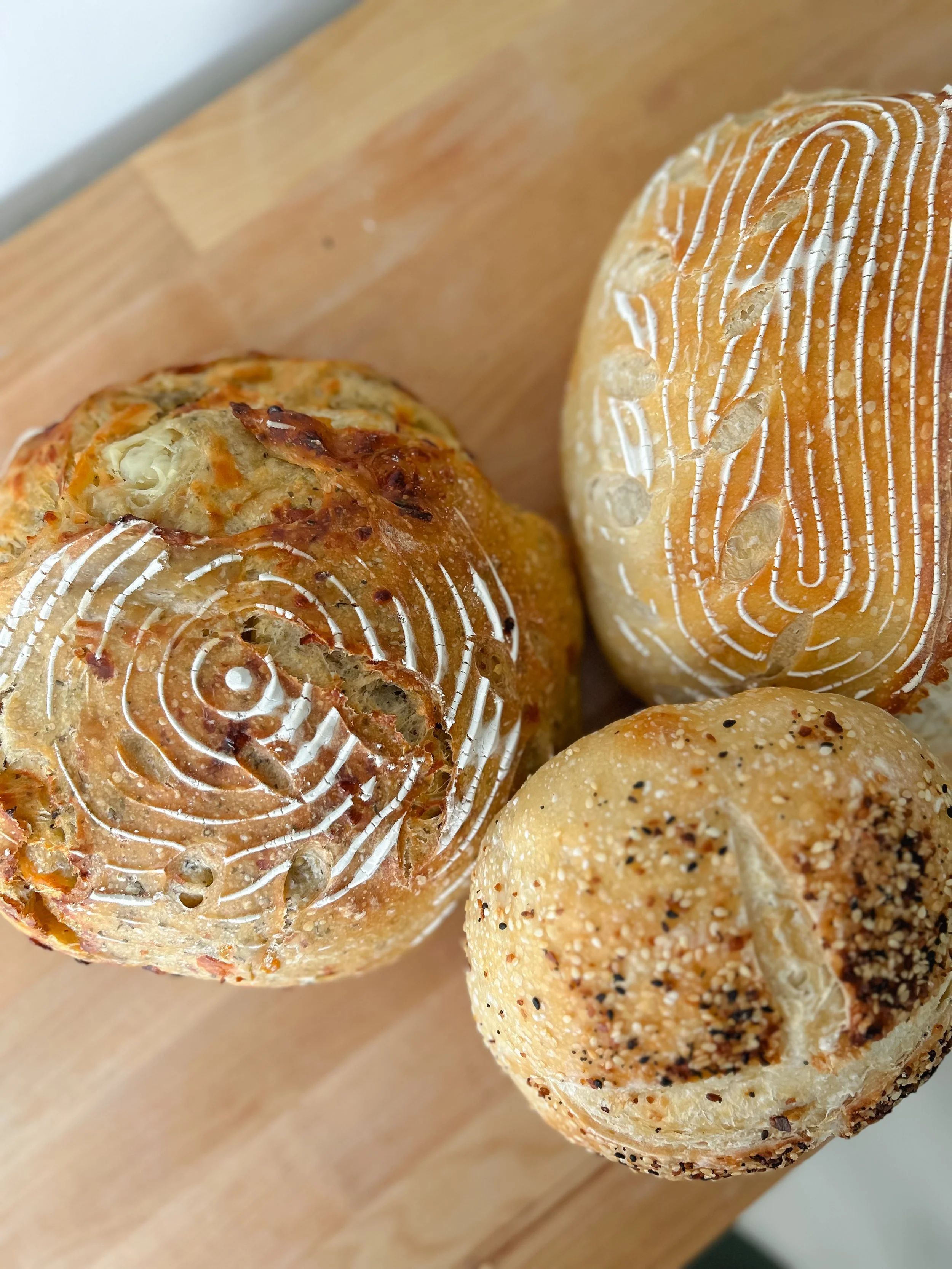Three assorted bread rolls on a wooden surface, one with white icing and twist patterns, one with seeds, and one with baked cheese topping.