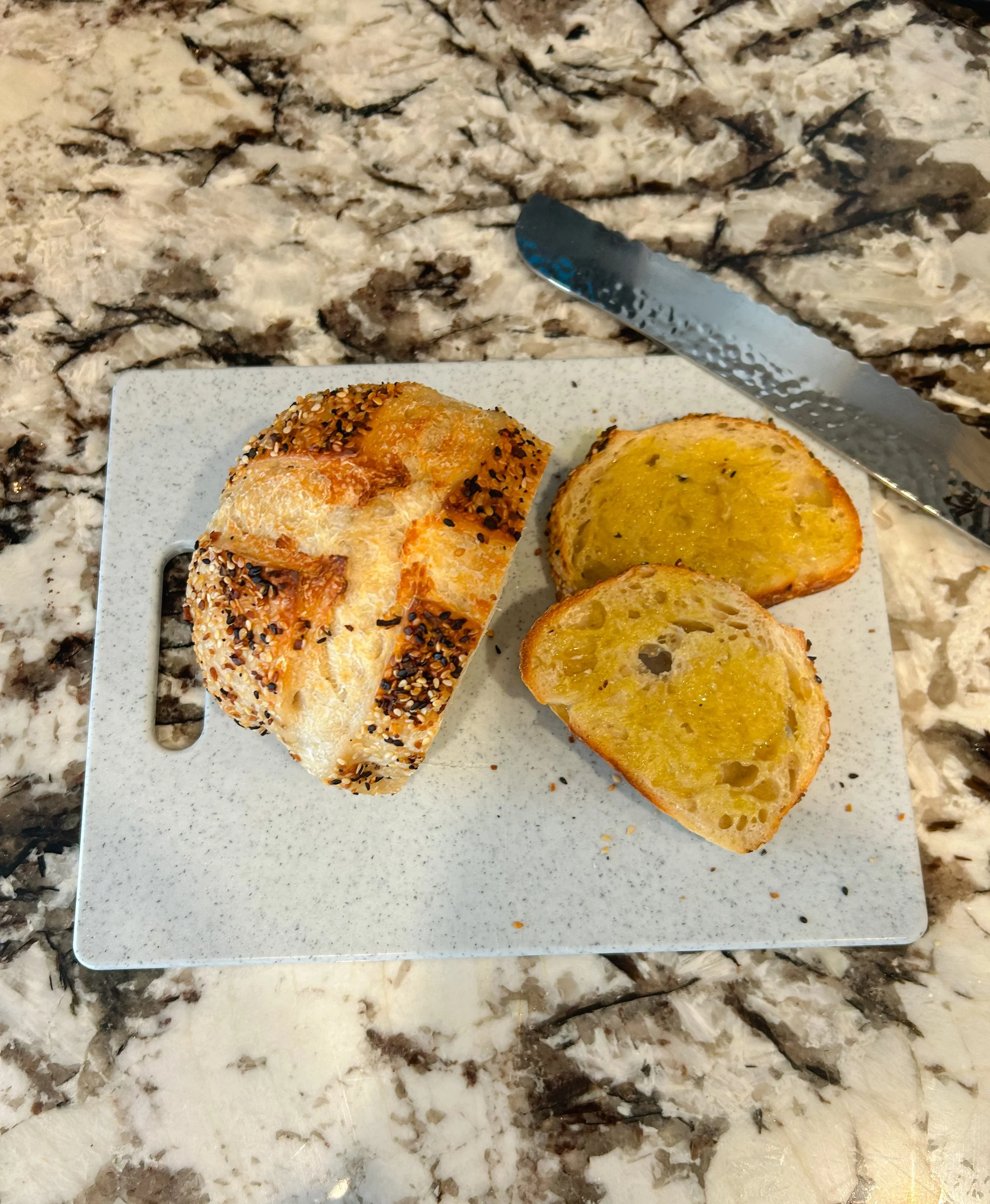 Bread roll with sesame and poppy seeds, two slices of garlic bread with melted butter, all on a white speckled plate on a marble countertop.