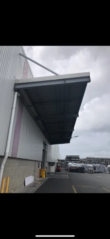 A large industrial building with an extended metal awning over a loading dock area with bird proofing