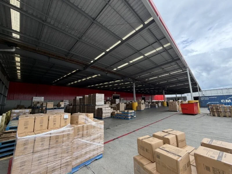 Warehouse with stacked cardboard boxes on pallets under a large metal roof showing a warehouse canopy with bird netting. Bird proofing to stop birds.