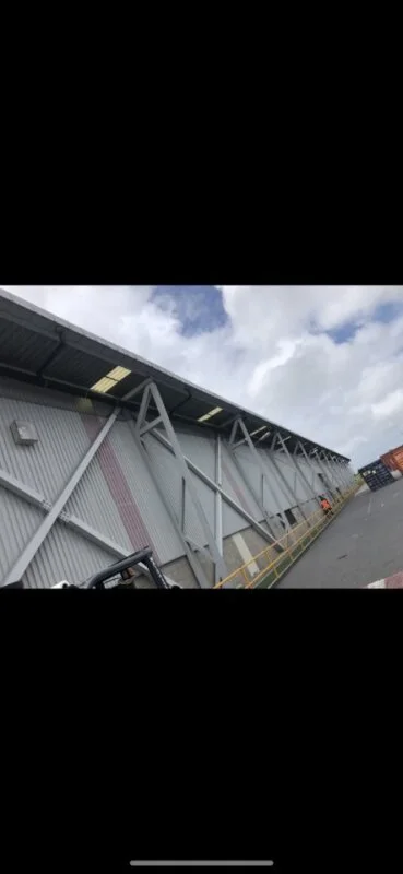 A large industrial building with a corrugated metal exterior and a sloped roof, with bird netting/proofing underneath to stop birds