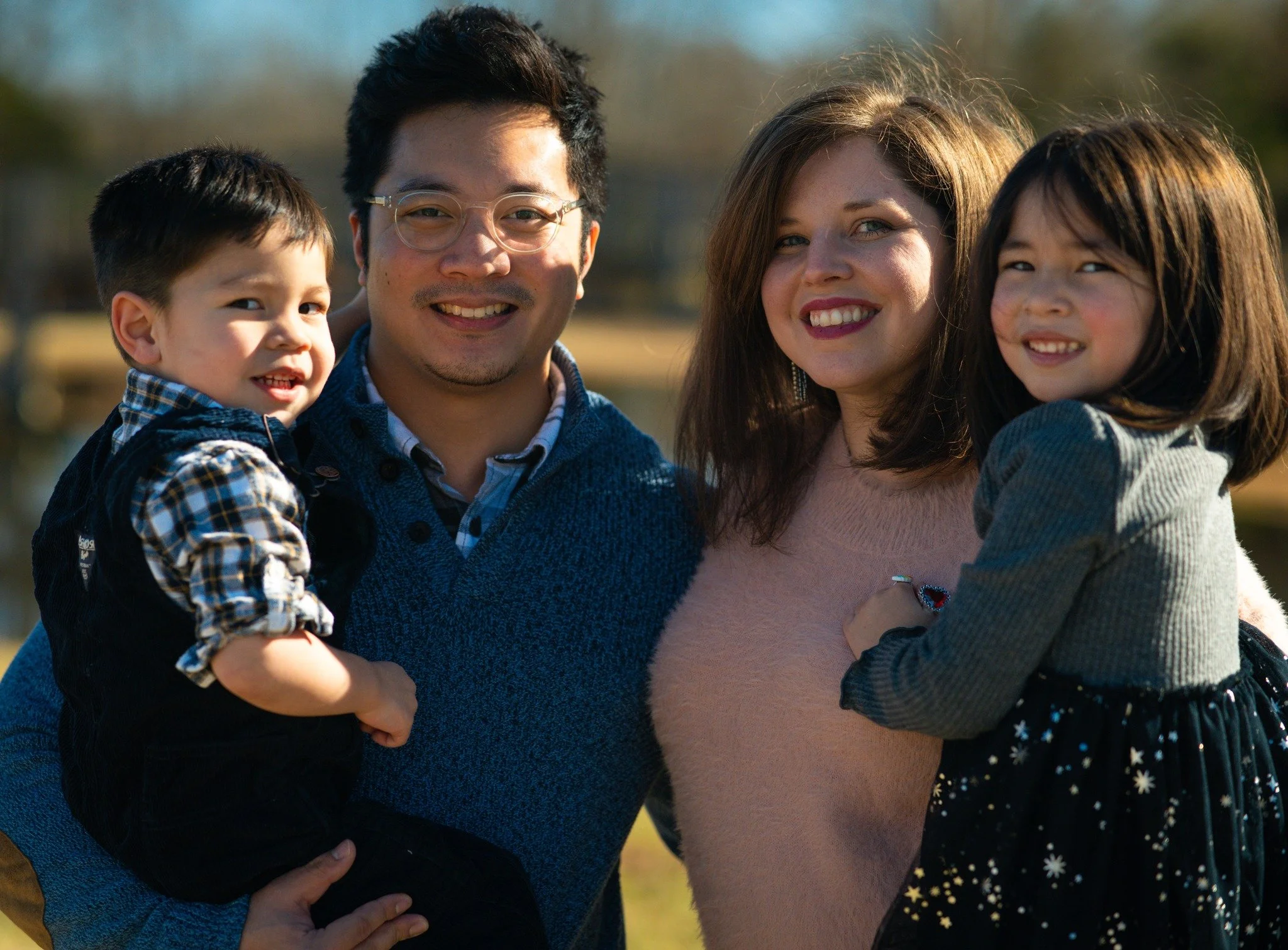 A diverse group of four people, two children and two adults, smiling and standing outdoors during daytime.