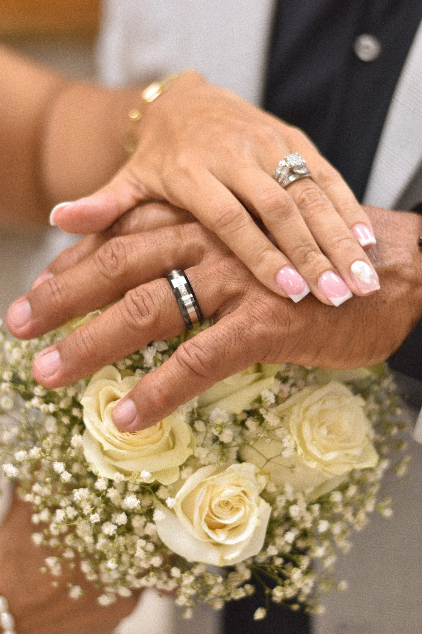 Close-up of a couple's hands with wedding rings resting on a bouquet of cream-colored roses and baby's breath.