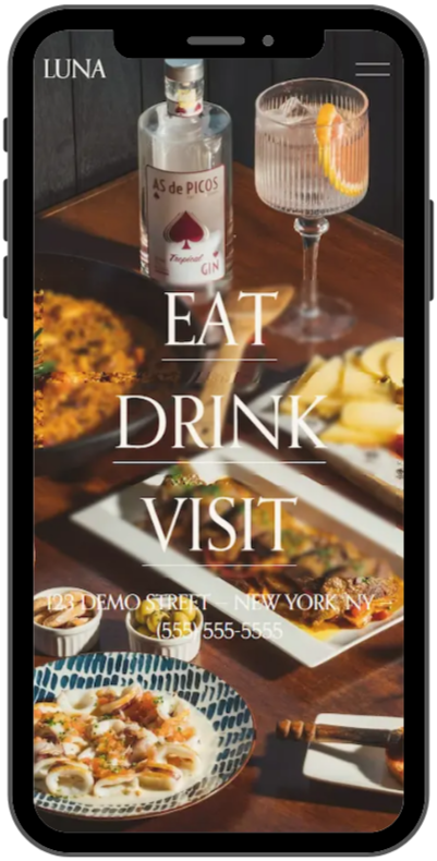A phone screen displays a restaurant's menu with food and drinks. The background shows a bottle of gin, a glass with a lemon slice, and various dishes including pasta and appetizers. Text on the screen reads "EAT DRINK VISIT" and includes the restaurant's address in New York.