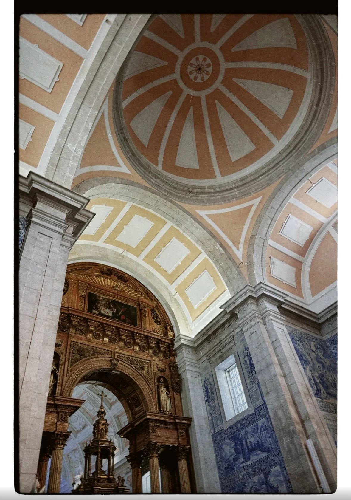 Interior de uma igreja com cúpulas decoradas, colunas de pedra, detalhes em madeira e azulejos azuis nas paredes.