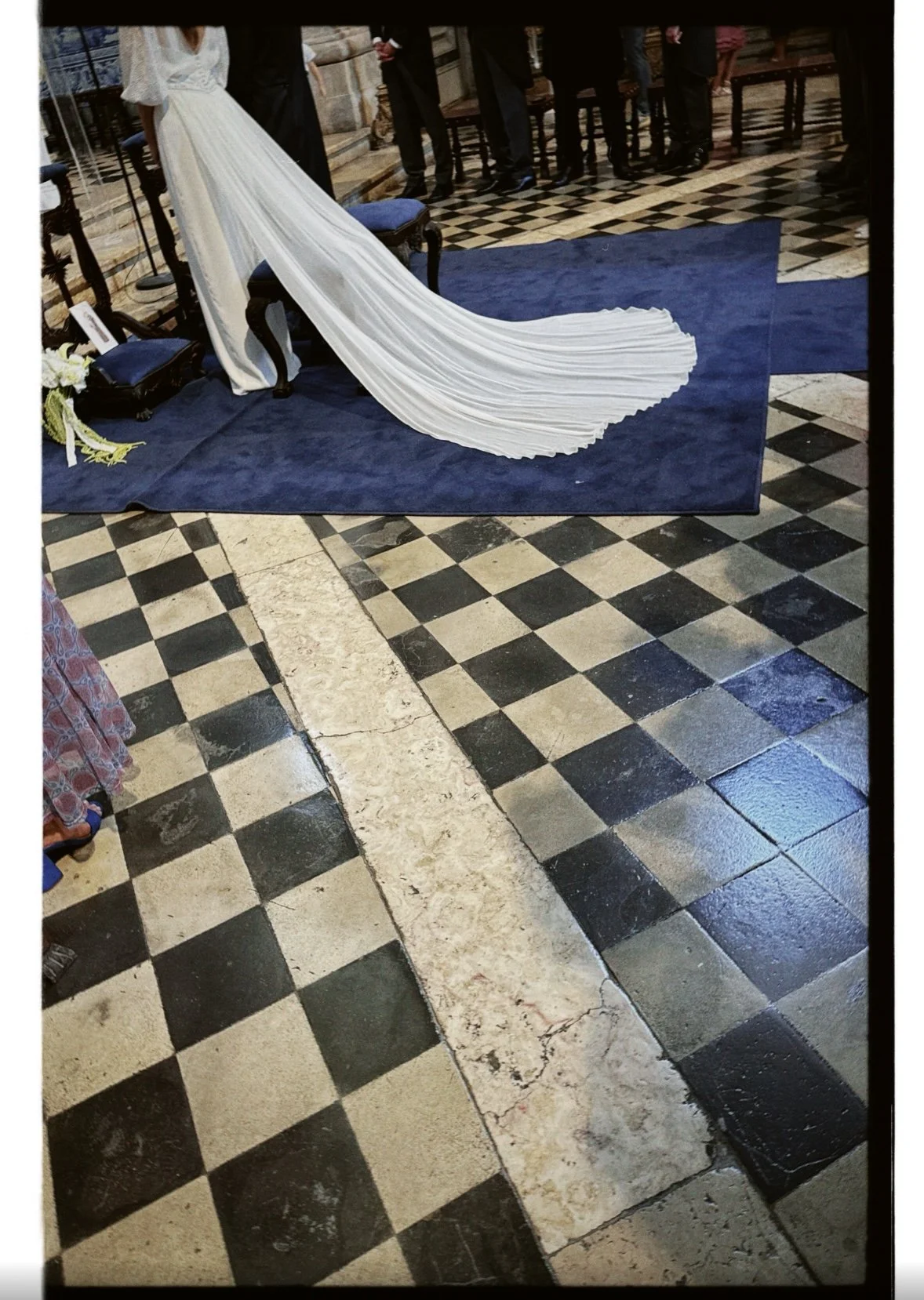 Decoração de casamento com a noiva de vestido branco e uma saia longa no altar, em uma igreja com piso de azulejos quadriculados preto e branco.