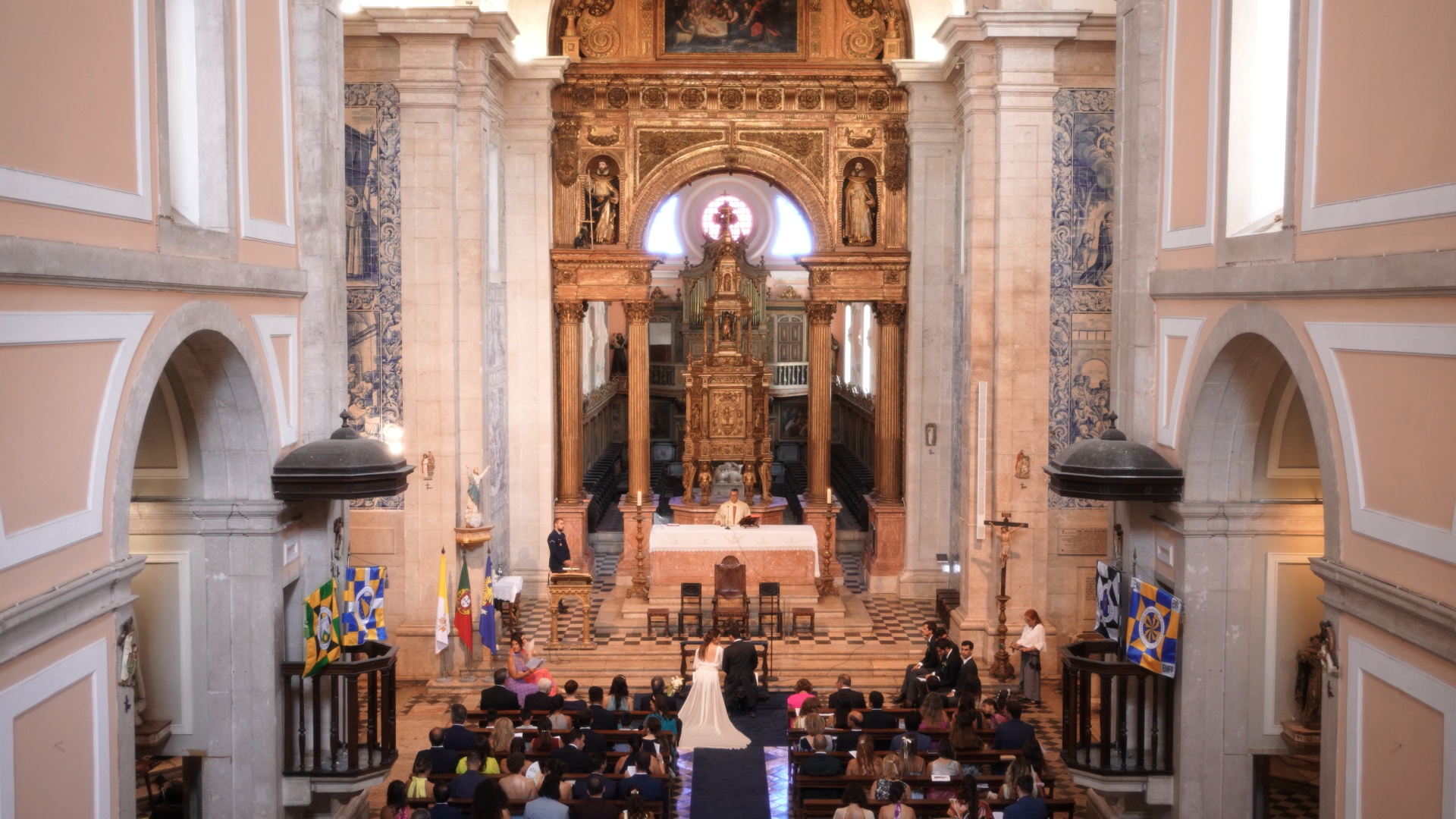 Cerimónia de casamento numa igreja em lisboa com convidados, casal de noivos, padre na frente e decoração tradicional