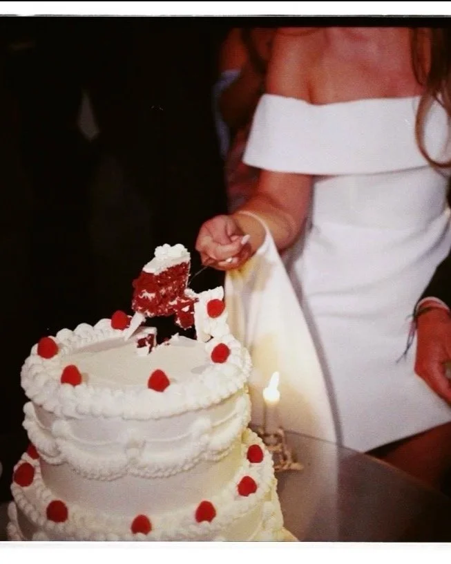 noivos cortando pedaço de bolo de casamento com cobertura branca e cerejas vermelhas