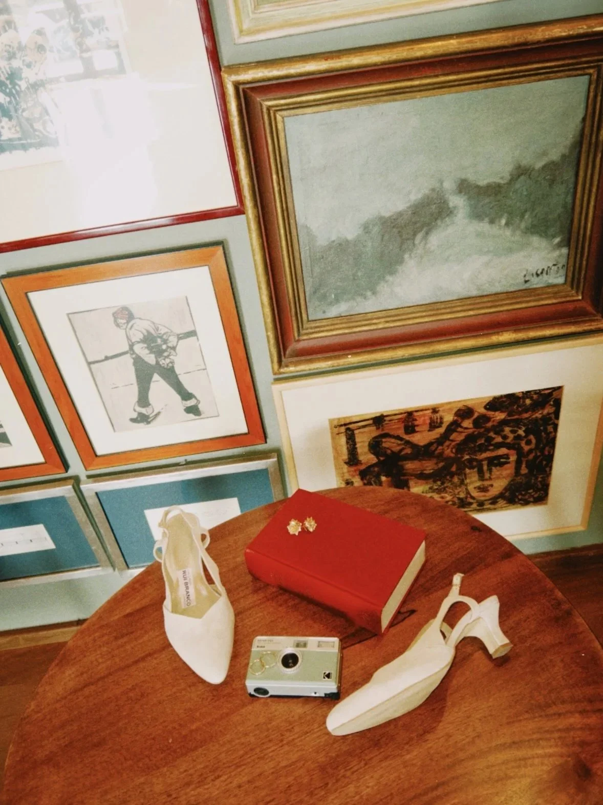 acessórios de noiva numa Mesa de madeira com um livro vermelho, um par de sapatos brancos femininos, uma câmera vintage e um par de brincos dourados, em Mafra
