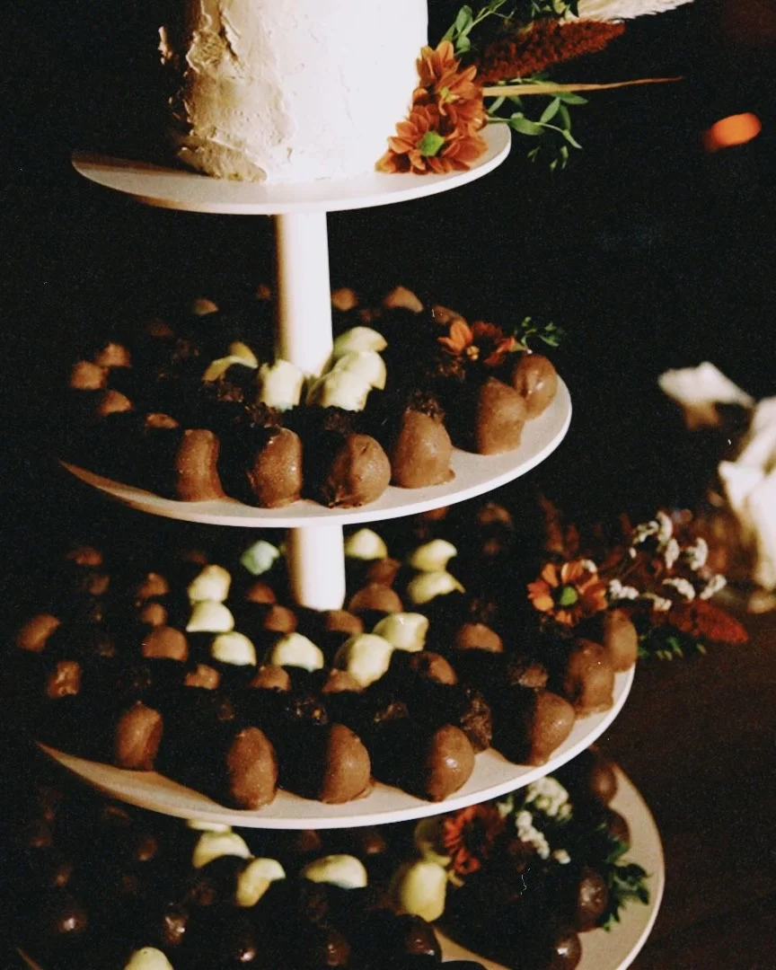 Bolo decorativo em um suporte de várias camadas, com Brigadeiro e outros doces ao redor, decorado com flores artificiais.