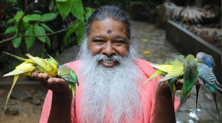 Sri Ganapathy Sachchidananda Swamiji smiling while feeding parakeets.