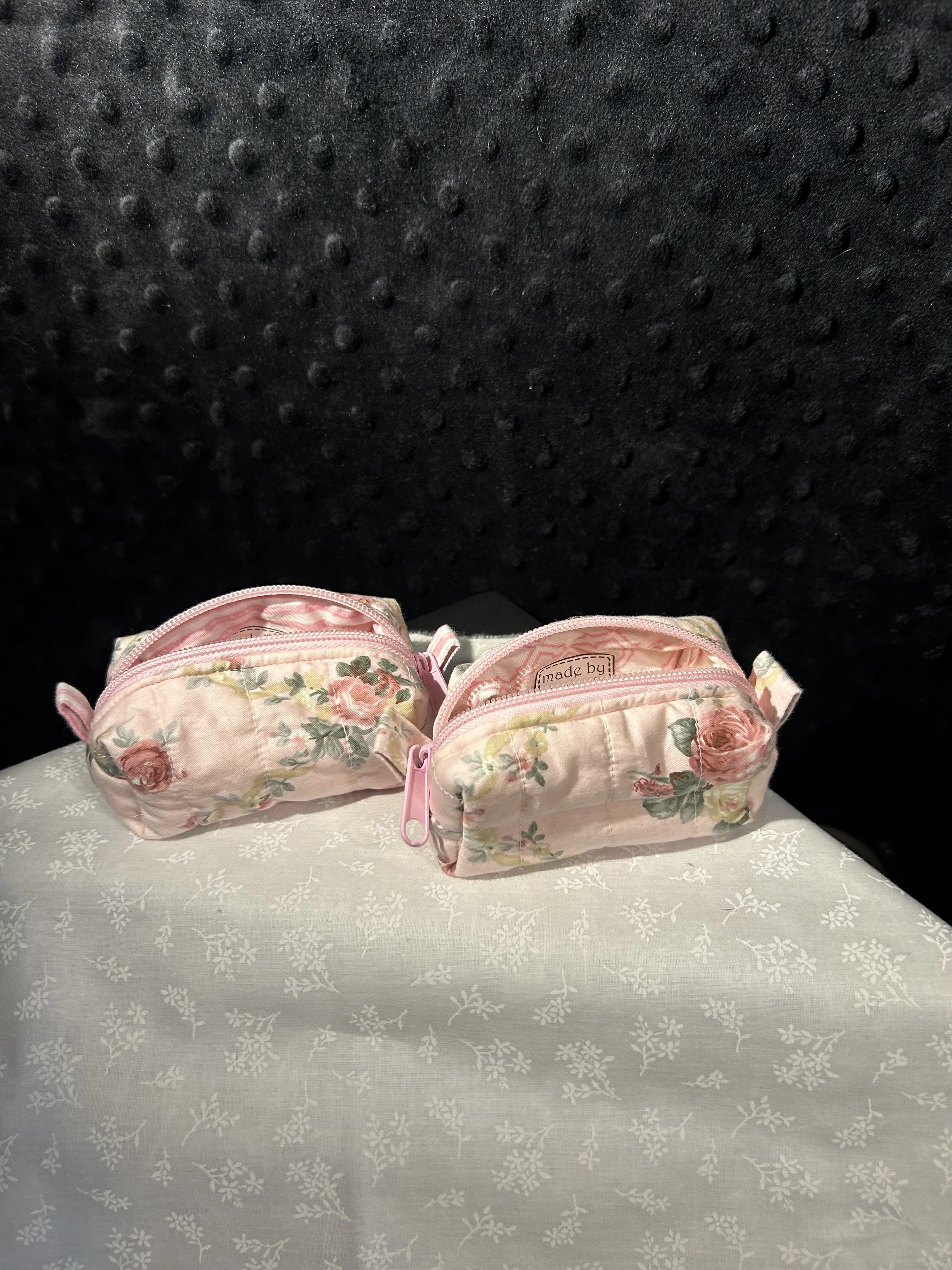 Two pink floral patterned zippered pouches on a white tablecloth with a black background.