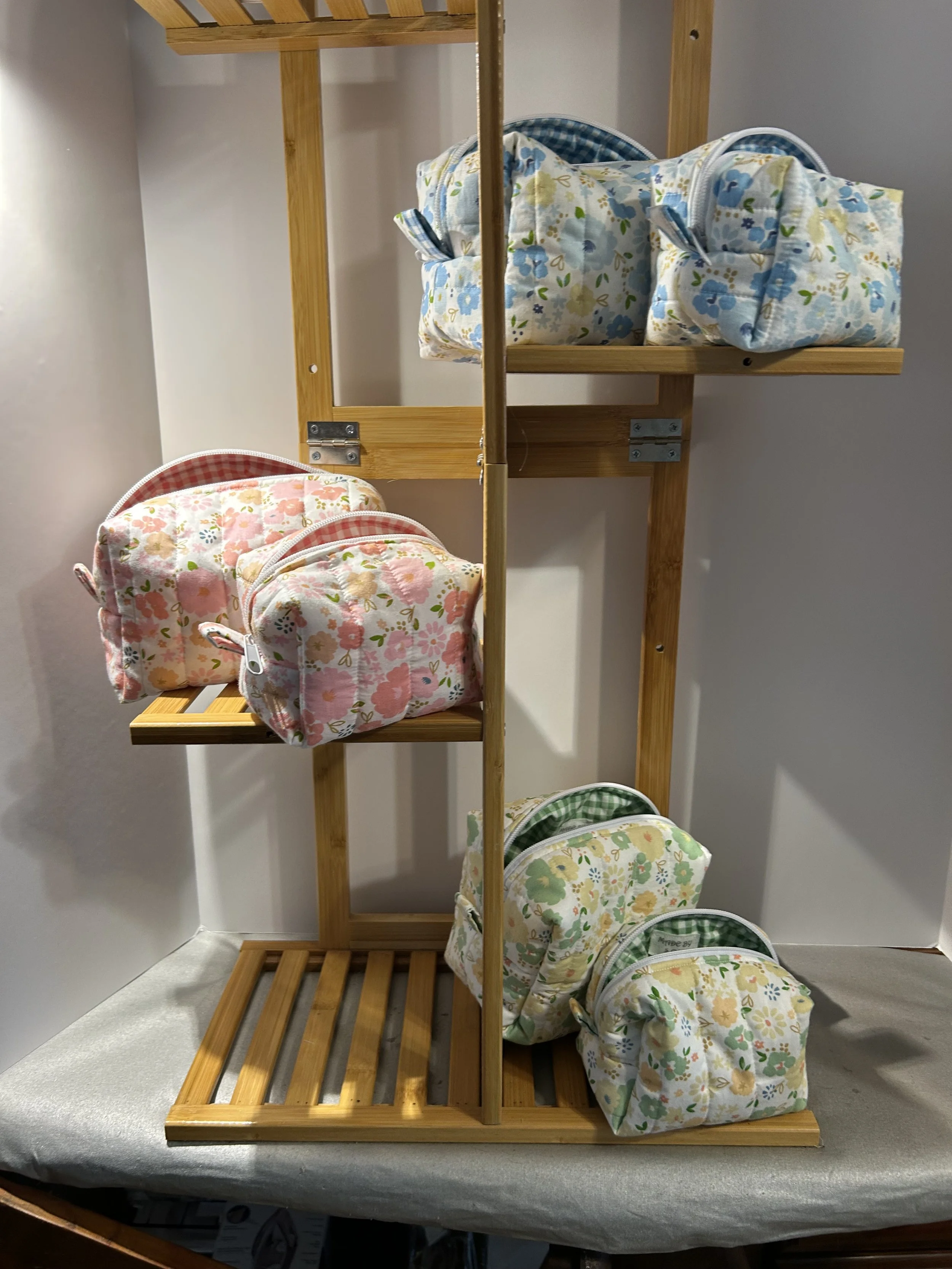 Wooden display shelf holding floral-patterned bags in pink, blue, and green designs.