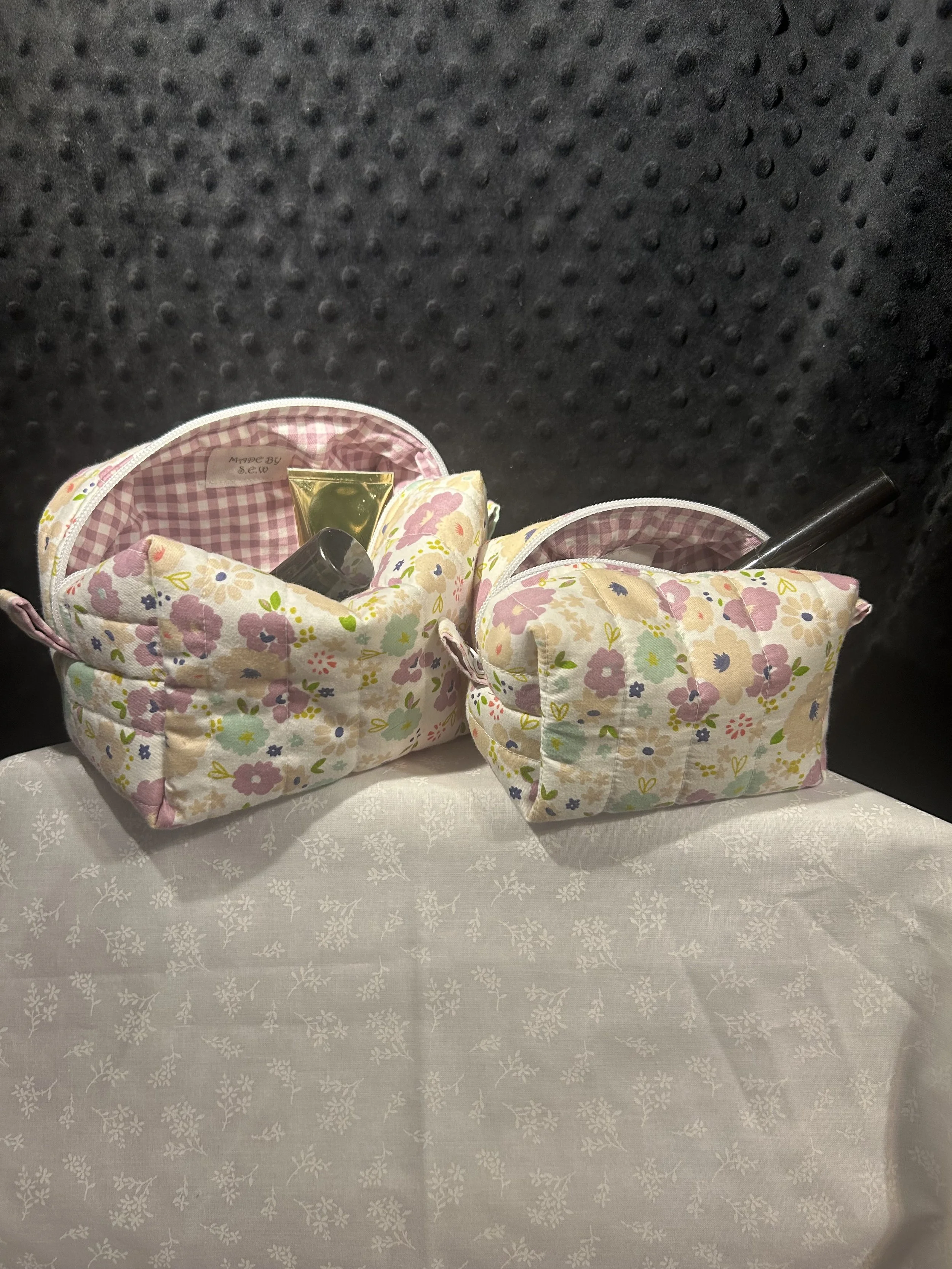 Two floral-patterned toiletry bags on a table with a white tablecloth, with various travel-sized toiletries inside.