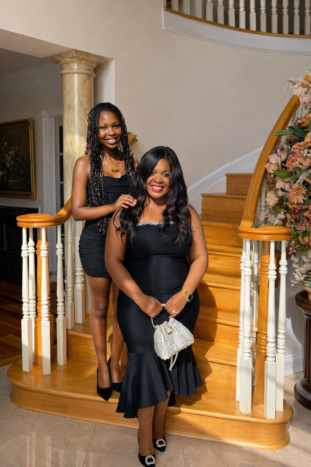 Two women dressed in black, smiling on a staircase with floral arrangements and wooden railings.