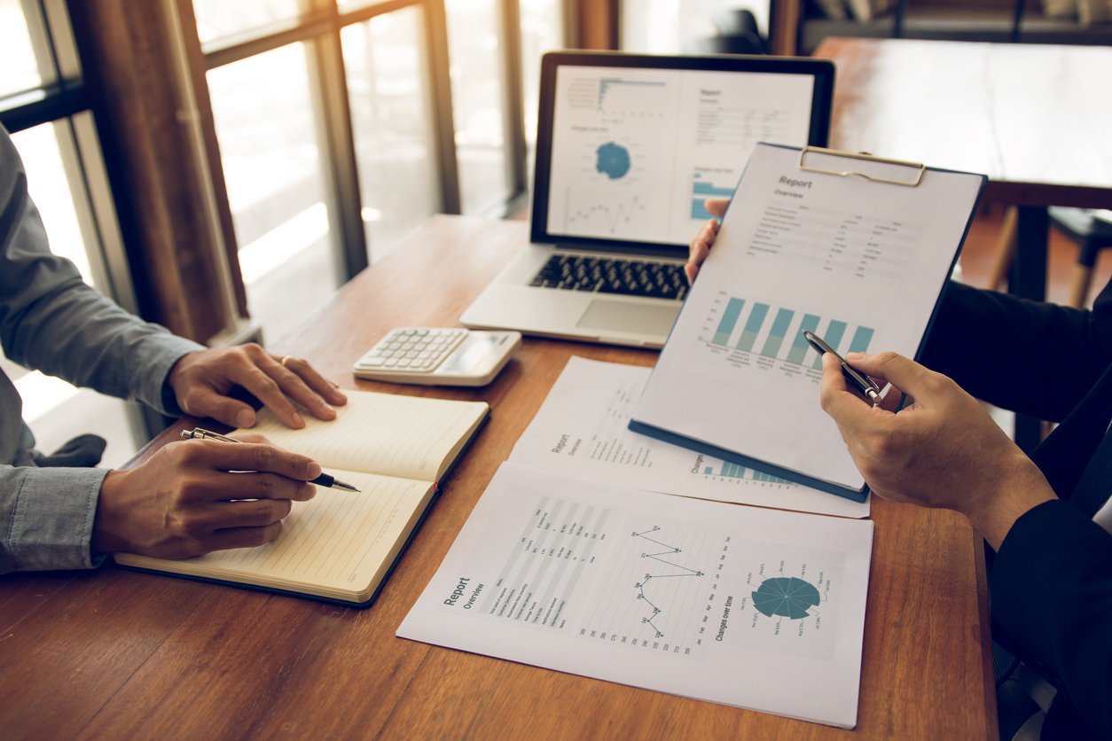 Dos personas en una reunión de negocios revisando informes y gráficos en una oficina.