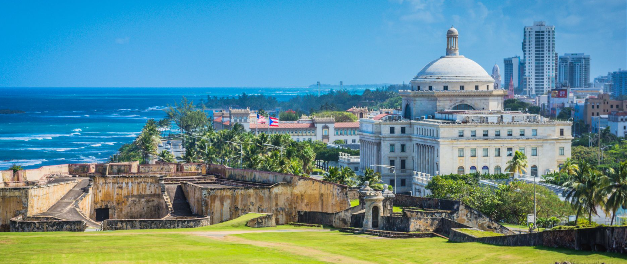 Vista panorámica de San Juan, Puerto Rico, con el mar al fondo y edificios modernos y antiguos en la ciudad.