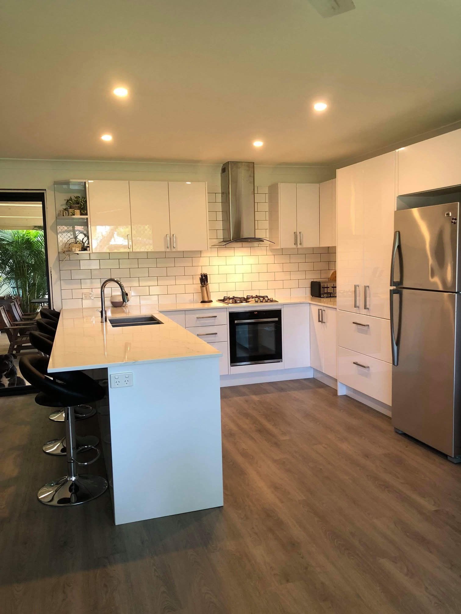 Modern kitchen with white cabinets, wooden floor, stainless steel appliances, island with seating, and white subway tile backsplash.
