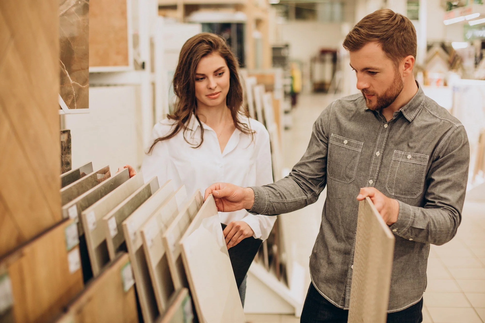 A young man and woman shopping for tiles at a store, examining sample tiles on display.