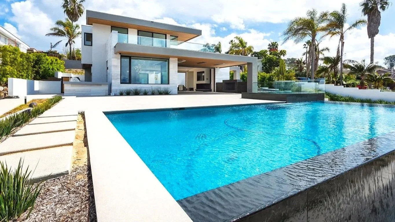 Modern house with large swimming pool and palm trees in backyard.