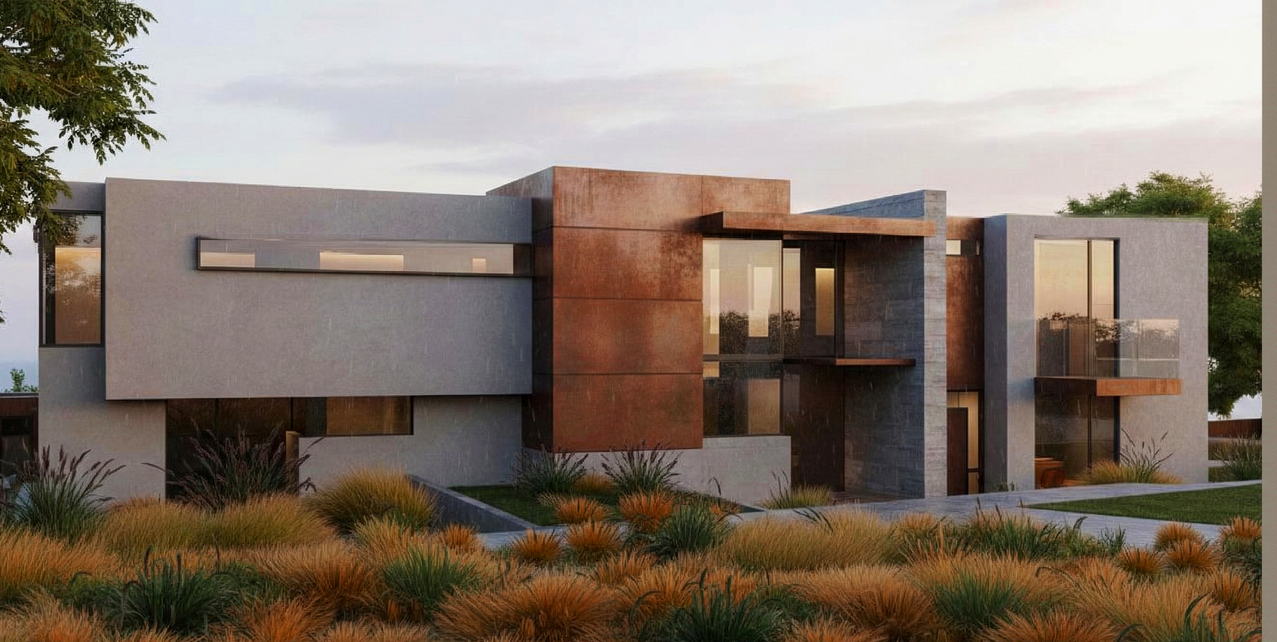 Modern two-story house with a flat roof, gray and rust-colored exterior walls, large windows, and glass balcony railings, surrounded by desert landscaping with grasses and plants.